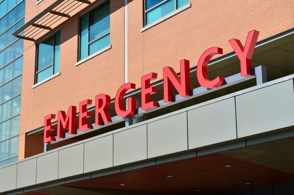 Why do the Marginalized wait longer in our ED's?? Close-up of a modern hospital emergency room entrance with prominent red letters.