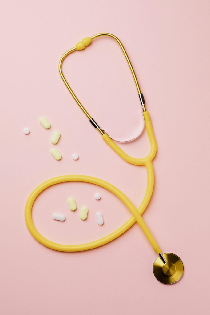 Joint Post- SDoH and ED's Flat lay of a yellow stethoscope and assorted pills on a pastel pink background.