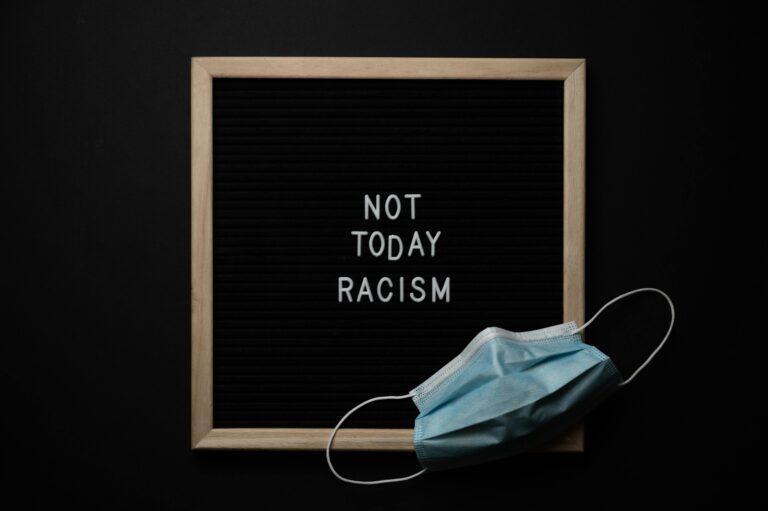 Overhead view of medical mask located on blackboard with white NOT TODAY RACISM inscription on center against black background
